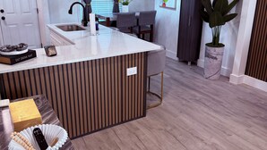 A modern kitchen with a central island, a dining area with chairs, a potted plant, and a wall with fruit illustrations. - 2-bedroom townhome in quaint Detroit with AC and comfort (Detroit)