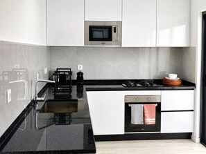 Uma cozinha moderna com armários brancos, bancada preta, micro-ondas embutido, máquina de café e fogão.