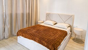 A modern bedroom with a large bed, two bedside tables, and a window with curtains. - Modern T2 apartment with rooftop pool (Praia)