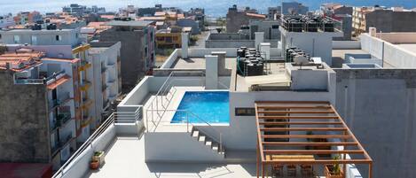 A rooftop with a swimming pool, outdoor seating, and a view of the sea.