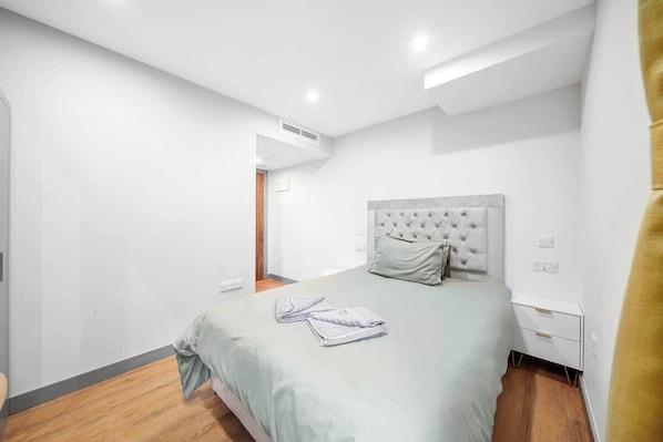 Une chambre à coucher comprenant un lit, une table de chevet, une bouche d’aération fixée au mur et une porte donnant sur une autre pièce.