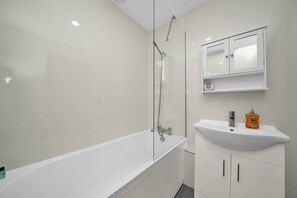 A modern bathroom with a bathtub, a sink, and a mirror cabinet. - Modern Studio 1 Min Walk to Ilford Station (London)
