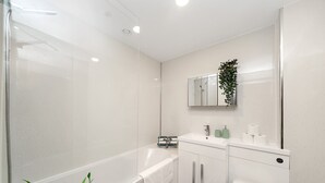A modern bathroom with a bathtub, a toilet, a sink, and a mirror. - Charming Studio 1 Min Walk to Ilford Station (London)