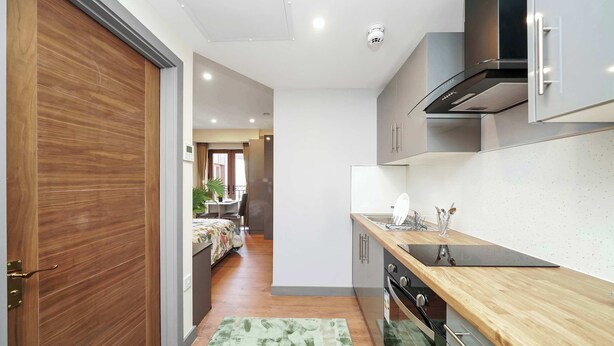 A modern kitchen with a wooden countertop, stainless steel appliances, and a view into the adjacent living area. - Charming Studio 1 Min Walk to Ilford Station (London)