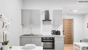 A modern kitchen with grey cabinets, a built-in oven, and a coffee maker. - Stylish Serviced Apartment w/ Rooftop Sky Bar (London)