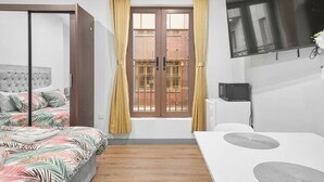 A bedroom with a bed, a desk, a television, and a window with curtains. - Stylish Serviced Apartment w/ Rooftop Sky Bar (London)