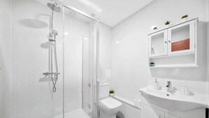 A modern bathroom with a glass-enclosed shower, a white toilet, and a white sink with a wooden cabinet above. - Stylish Serviced Apartment w/ Rooftop Sky Bar (London)