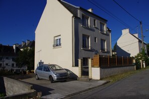 A two-story residential building with a parked car in the driveway. - Apartment in house with garden 5 min from beaches. Beds made up on arrival. (Audierne)