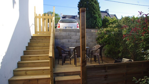 Un escalier en bois mène à un espace patio aménagé avec du mobilier d’extérieur.
