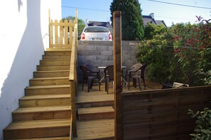 Eine Holztreppe führt zu einer Terrasse mit Gartenmöbeln.