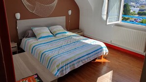 Une chambre à coucher avec un lit, des tables de chevet, une moustiquaire suspendue, une fenêtre donnant sur un paysage agréable et un radiateur.