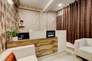 A reception area with a marble wall, a wooden reception desk, a potted plant, a sign, and a white sofa. - Single Room Dwarka Aakarshan Residency (New Delhi)