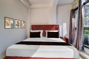 A hotel room with a large bed, a nightstand, a window with curtains, and three framed artworks on the wall. - Single Room Dwarka Aakarshan Residency (New Delhi)