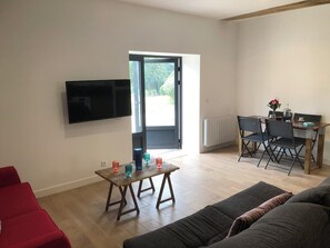 Ein modernes Wohnzimmer mit Flachbildfernseher, einem Holzessttisch mit Stühlen und einer Couch.