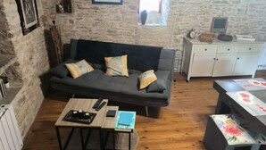 A cozy room with a stone wall, a dark sofa, a wooden coffee table, and a small cabinet with a TV. - Lot house in Bouriane (Thédirac)