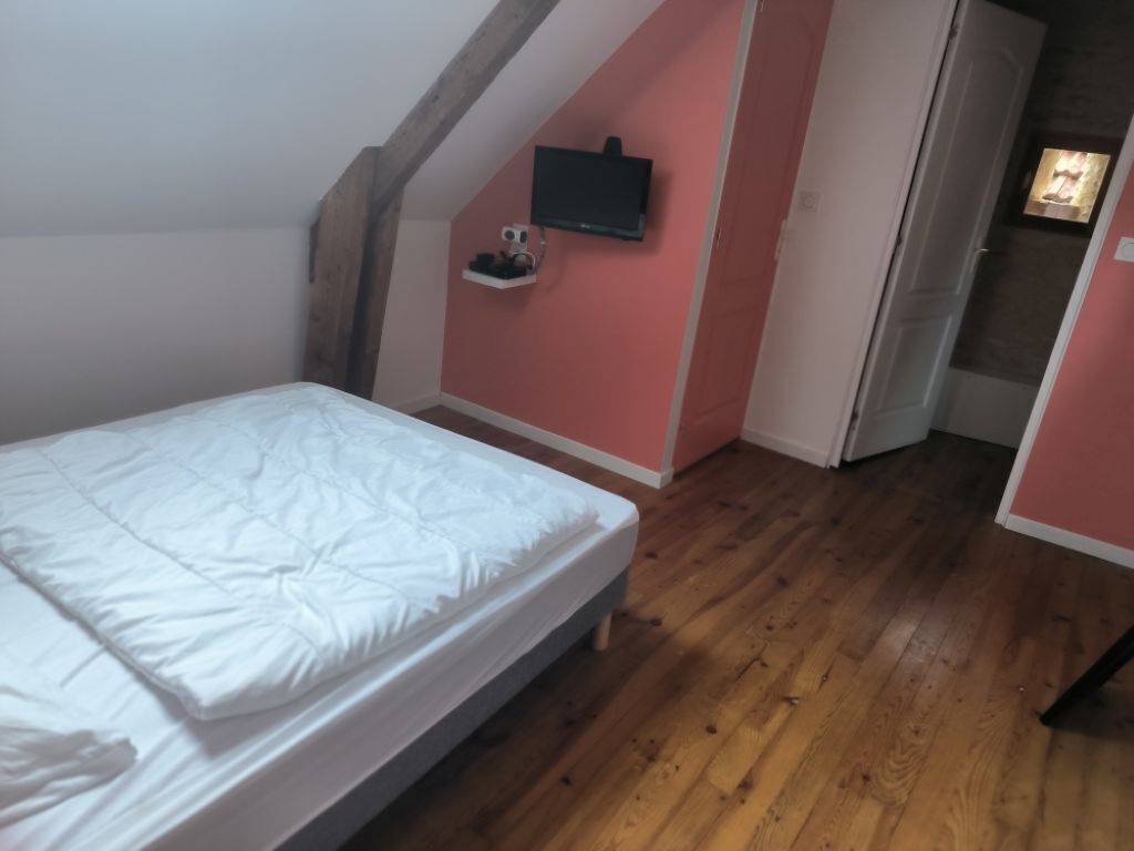 Un dormitorio con cama, piso de madera, televisor montado en la pared y una puerta que da a otra habitación.