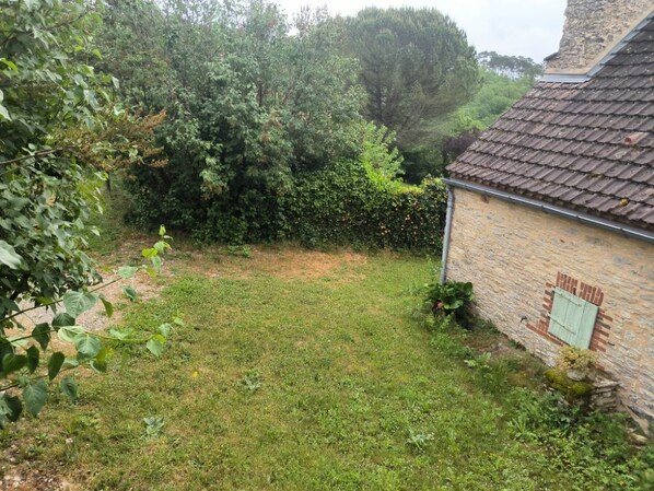 A grassy yard with a brick building, a stone wall, and dense foliage.