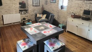 A rustic room with stone walls, a wooden floor, a black sofa, a dining table with floral cushions, a white cabinet, and a window with a view. - Lot house in Bouriane (Thédirac)