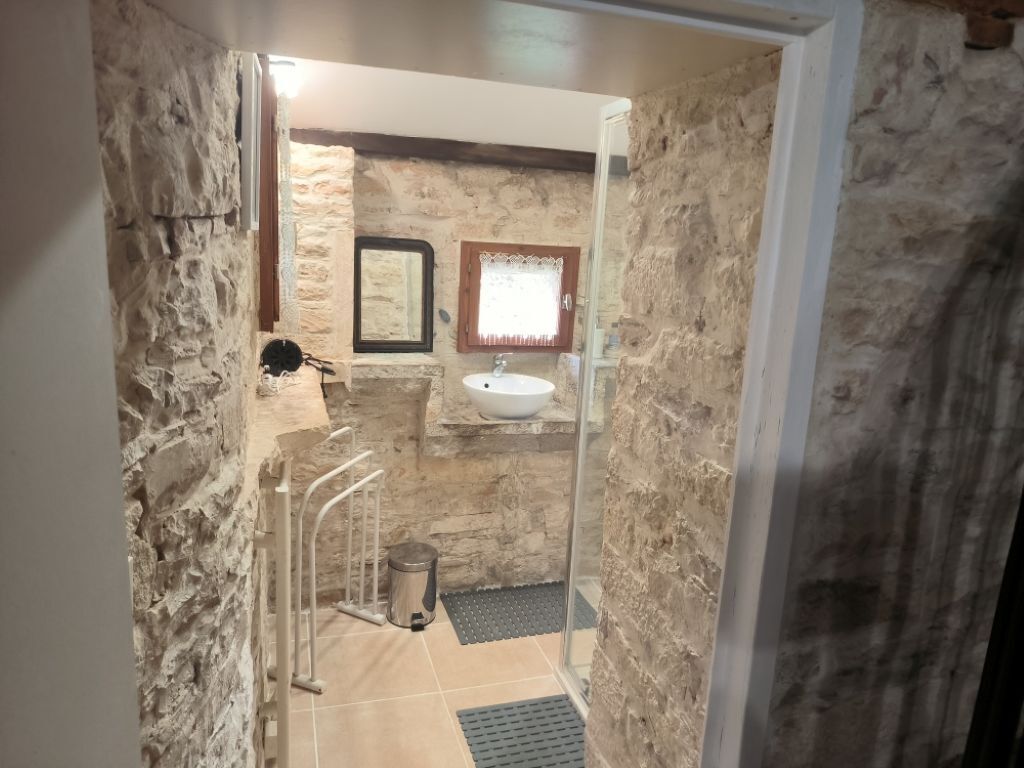 Ein Badezimmer mit Steinwänden, einem weißen Waschbecken, einem Spiegel und einer Duschkabine.