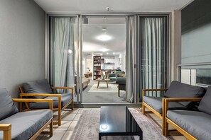 A living room with a sofa set, a coffee table, and a sliding glass door leading to a dining area. - Stylish Apartment w/ Balcony, Pool & Gym (Brisbane City)