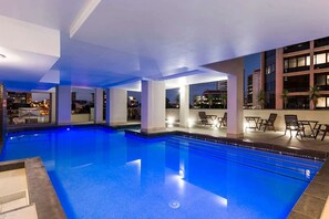 A swimming pool with lounge chairs and a view of the cityscape at night. - Stylish Apartment w/ Balcony, Pool & Gym (Brisbane City)