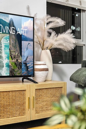 A television displaying 'LIVING ART' with a vase of pampas grass on a wooden cabinet. - Stylish Apartment w/ Balcony, Pool & Gym (Brisbane City)