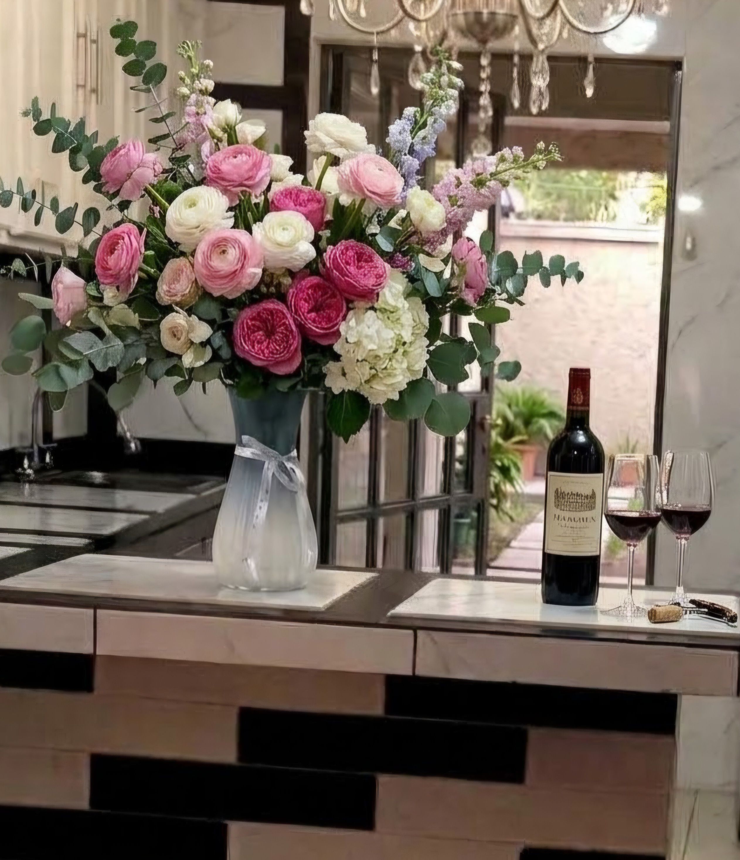 Una encimera de cocina con un florero, una botella de vino y dos vasos.