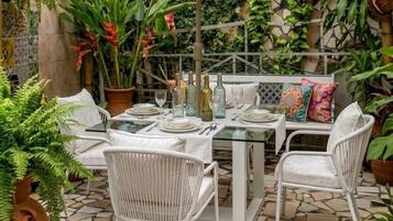 Un patio exterior con una mesa lista para comer, rodeado de sillas de mimbre blanco y una sombrilla.