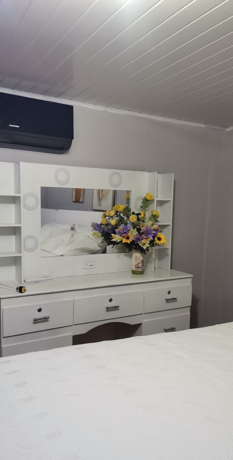 A bedroom with a white dresser, a mirror, and a vase of flowers.
