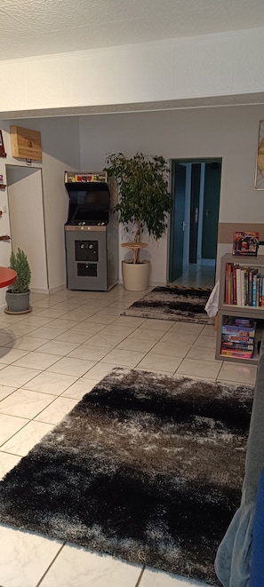Een woonkamer met een open haard, een potplant, een boekenkast en een deur naar een andere kamer.