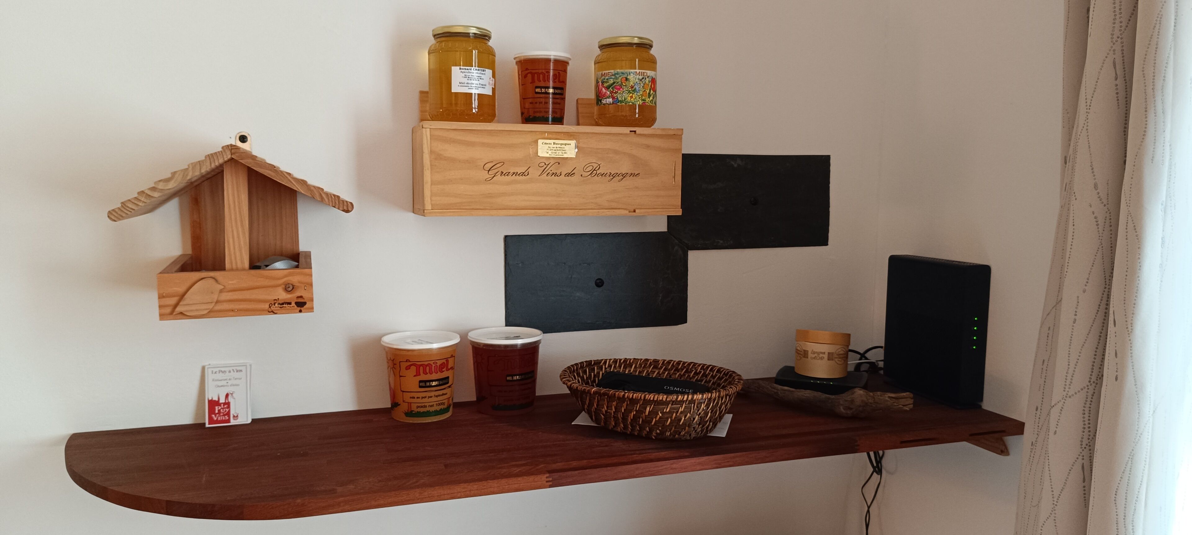 Een houten plank met potten honing, een rieten mand en een vogelhuisje van hout.
