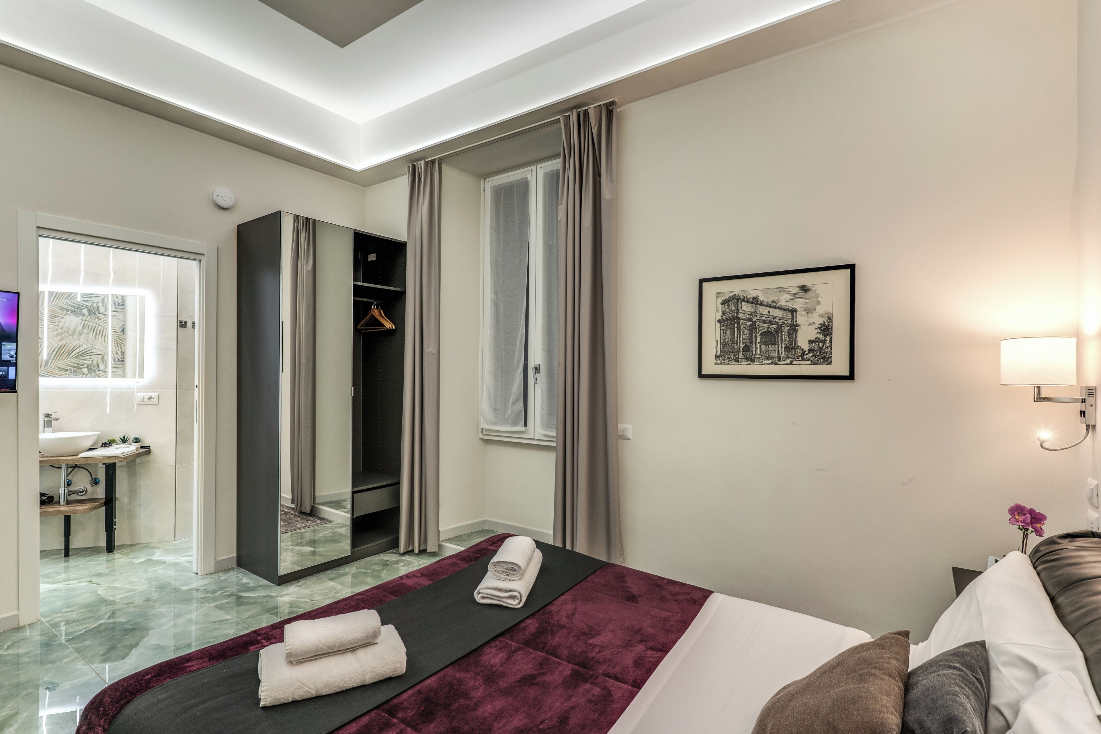 A hotel room with a bed, a mirror, a wardrobe, a bathroom, and a framed picture on the wall.