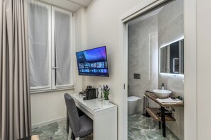Um banheiro moderno com um espelho grande, pia e vaso sanitário. Há uma televisão na parede exibindo um aplicativo VIM.