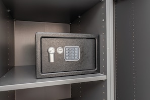 A safe with a keypad and a keyhole, placed on a shelf in a room with a plain wall and a metal frame. - Adriana 5 Luxury rooms (Rome)