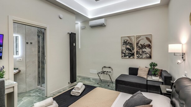 A modern hotel room with a bed, a seating area, a shower, and artwork on the walls. - Adriana 5 Luxury rooms (Rome)