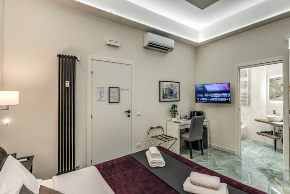 A hotel room with a bed, a desk, a chair, a TV, and a bathroom visible through an open door. - Adriana 5 Luxury rooms (Rome)