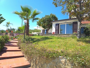A residential property with a stone pathway, a lawn, and a modern house with large windows and shutters.