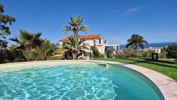 A swimming pool with clear water, surrounded by lush greenery and a white building with a red roof. - Oasis Villa - Villa with pool and private giarino, San Remo (Sanremo)