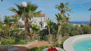 A poolside area with a table set for dining, surrounded by lush greenery and a view of the sea. - Oasis Villa - Villa with pool and private giarino, San Remo (Sanremo)