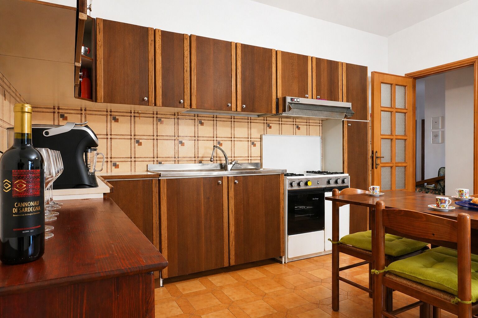 A kitchen with wooden cabinets, a gas stove, a sink, and a dining area with a chair.