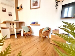 Ein Wohnzimmer mit Holzboden, zwei Korbstühlen, einem Fernseher und einem Bücherregal.