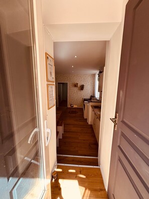 A narrow hallway leading to a kitchen area with wooden flooring, a small table, and a door on the right. - Marea Cosy Terrace All-Inclusive, Mourillon Center (Toulon)