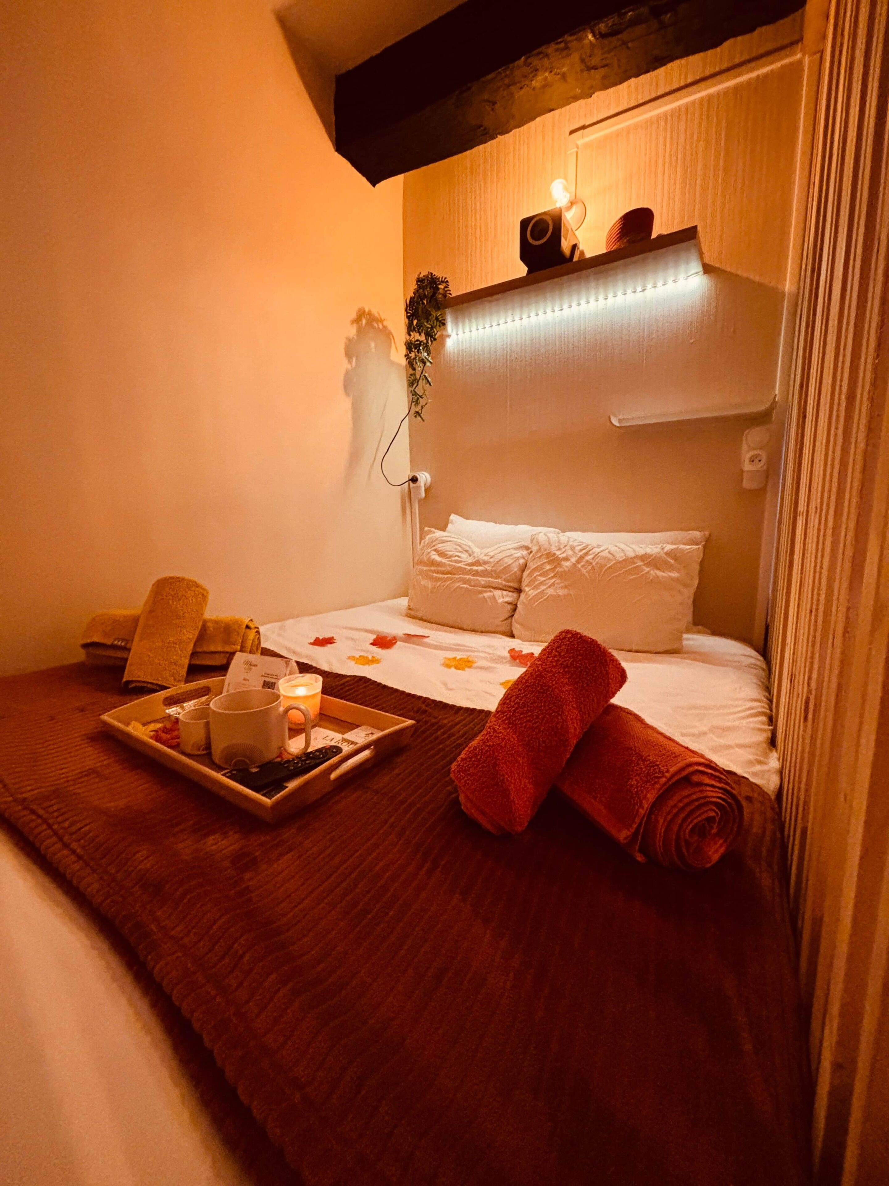 Een hotelkamer met een bed, een nachtkastje met een dienblad met ontbijtartikelen, een opgerolde handdoek en een wandluidspreker.
