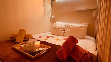 Een hotelkamer met een bed, een nachtkastje met een dienblad met ontbijtartikelen, een opgerolde handdoek en een wandluidspreker.