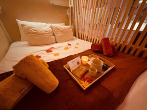 A hotel room with a neatly made bed, a tray with a candle, a book, and a mug.