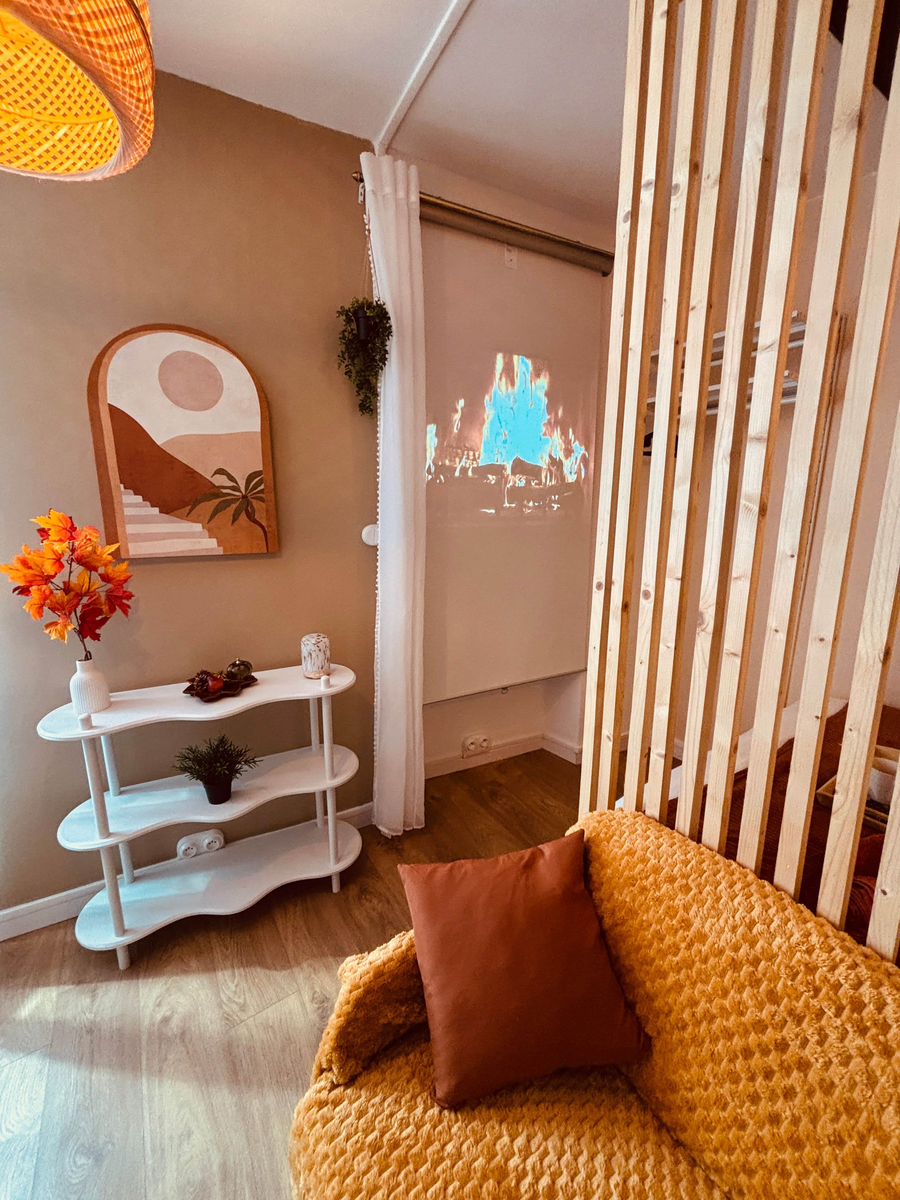 Ein gemütliches Zimmer mit einer Couch, einem weißen Regal mit Dekoration, einem Wandbild und einer Projektion einer Kamin-Szene.