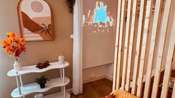 A cozy room with a sofa, a white shelf with decorative items, a wall-mounted painting, and a projection of a fire scene.