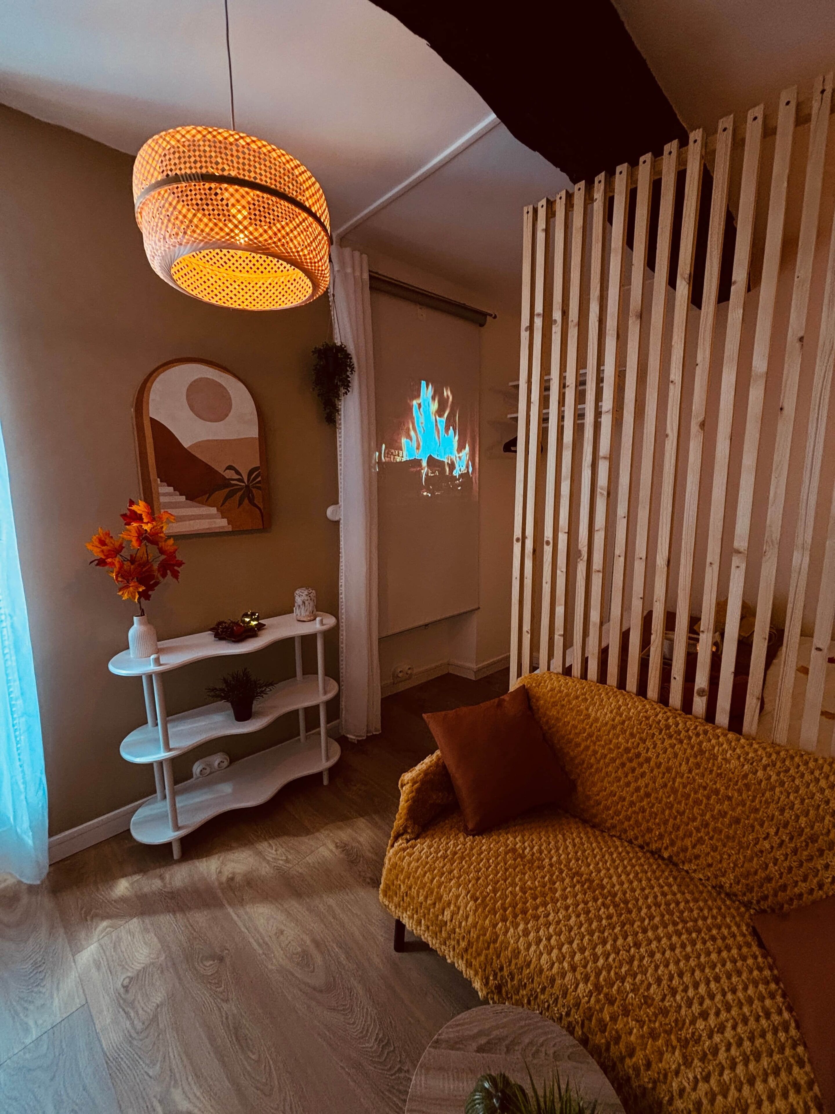 Een woonkamer met een bank, een wandplank, een hanglamp en een projectiescherm waarop een vuur wordt getoond.