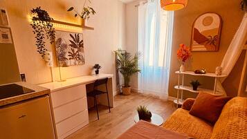 Un espace de vie compact comprenant un coin cuisine, un coin repas et un coin salon avec un canapé et un fauteuil.