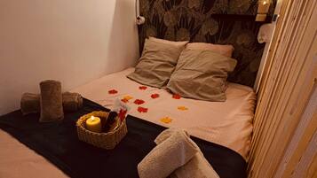 A bedroom with a bed, a wall-mounted light, a small shelf with a plant, and a decorative wall.